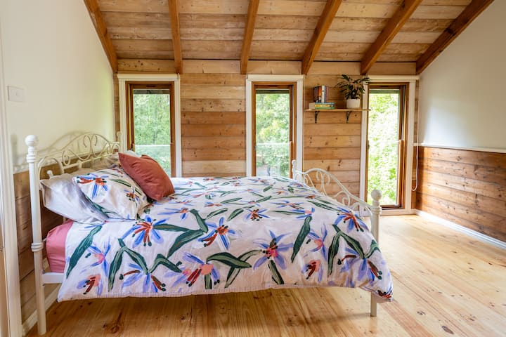 This bedroom is located upstairs and has giant round circular windows at either end. It is a spacious room with a side window view of the property and balconies either end to step out and enjoy the fresh air and beautiful views.
