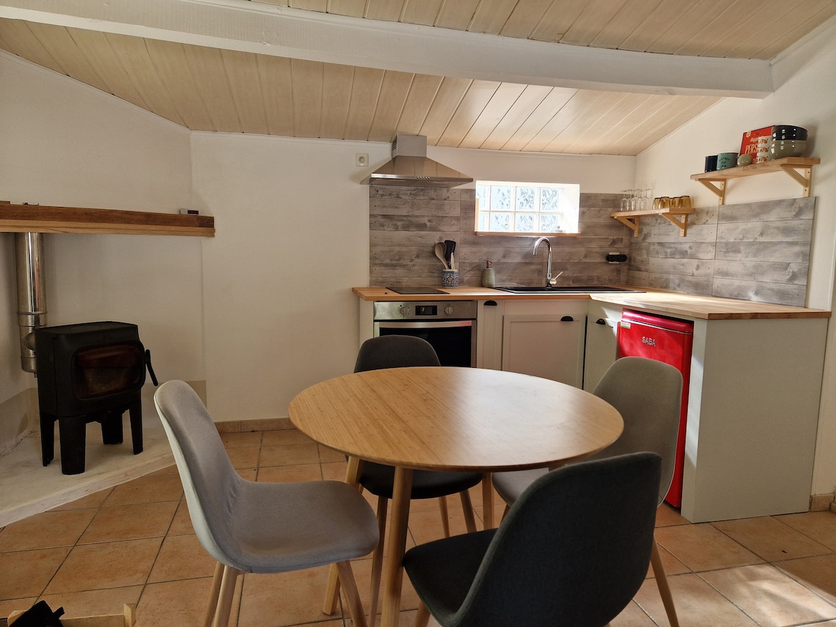 The kitchen area features sleek cabinetry and a red refrigerator. It includes a round dining table surrounded by four chairs. A small wood-burning stove is positioned in one corner, enhancing the overall functionality of the space.