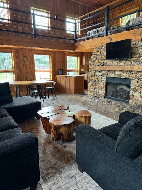 A cozy living area features a stone fireplace, with a mounted television above. Two dark sofas are positioned around a unique wooden coffee table, while a dining table with chairs is visible in the background, accompanied by a well-equipped kitchen area.