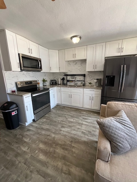 The modern kitchen features sleek white cabinetry and stainless steel appliances, including an oven, stove, and refrigerator. Counter space is organized with a coffee maker and decorative plants. A cozy seating area with a neutral-colored sofa is positioned nearby, enhancing the home's functionality.