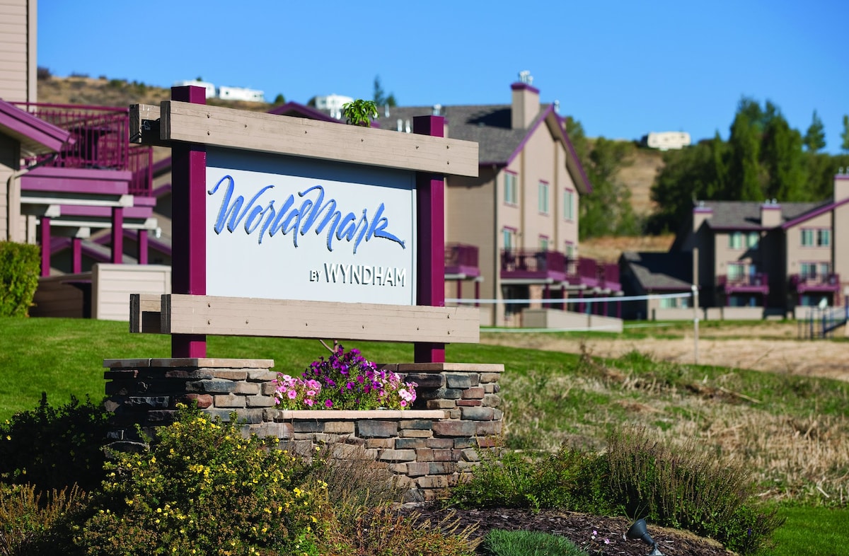 A welcoming entrance sign for WorldMark by Wyndham is set against a backdrop of landscaped greenery and resort buildings. The sign is adorned with purple and gray tones, providing a distinctive identity to the location. Nearby, well-maintained features enhance the overall setting.