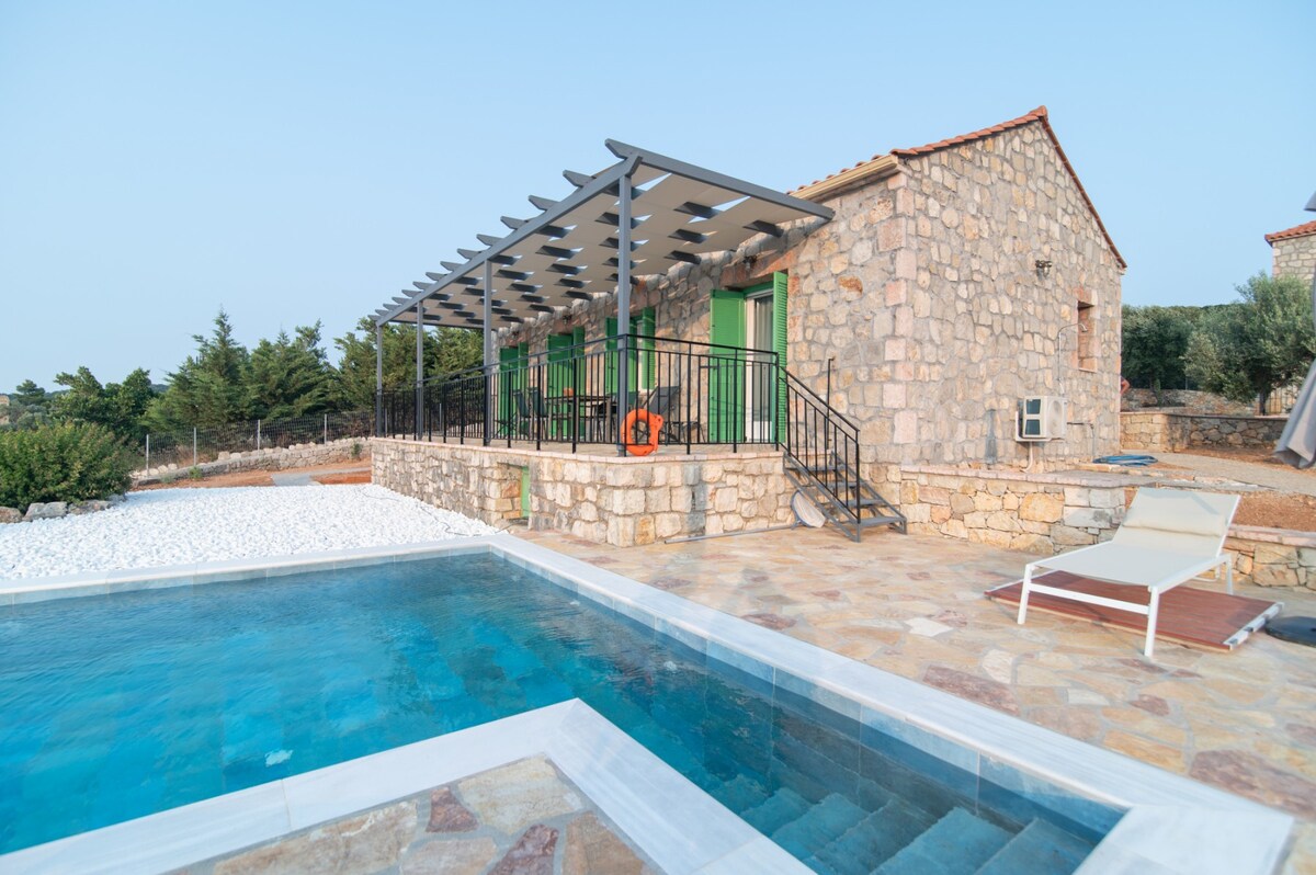 A charming stone villa is complemented by a private swimming pool with a shallow entry. A covered terrace provides shaded seating, and lush greenery surrounds the property, contributing to a serene outdoor environment.