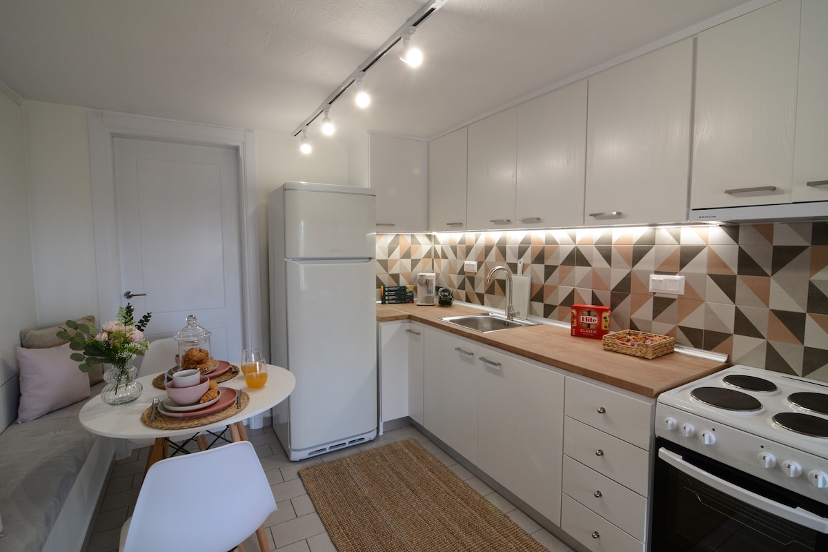 A fully equipped kitchen features modern appliances, including a refrigerator and stove. A light wood countertop provides preparation space, while a geometric tile backsplash adds visual interest. A small dining area is present, accompanied by a round table set with dining ware and decorative touches.