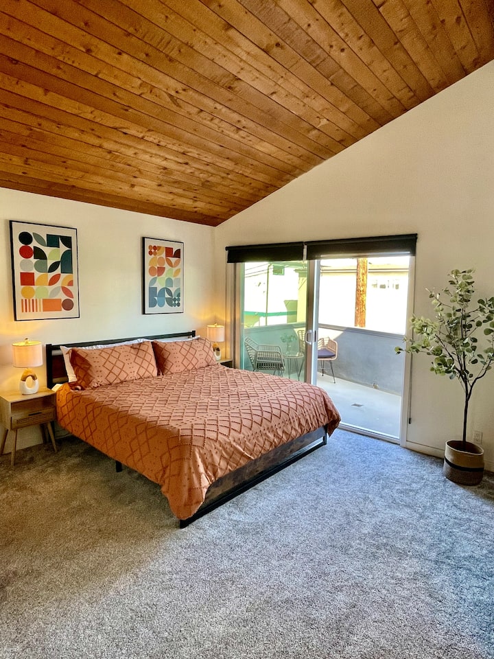 Ova topla spavaća soba ima svodni drveni strop, bračni krevet i elegantan unutarnji kamin. Klizna staklena vrata koja vode do privatne  terase ispunjavaju prostor prirodnim svjetlom. Moderni ukrasi, sivi tepih i uokvirena umjetnička djela dodaju stil.