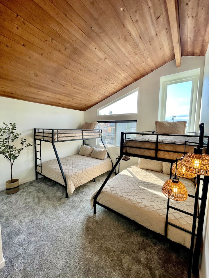 Udobna soba na kat s dva crna kreveta na kat s metalnim okvirom, od kojih svaki ima donji dio bračnog kreveta i dvostruki gornji dio. Topli drveni strop u kontrastu je s modernim prozorima, mekim tepisima i neutralnom posteljinom. Tkana viseća svjetla i biljka u tegli daju šarm.