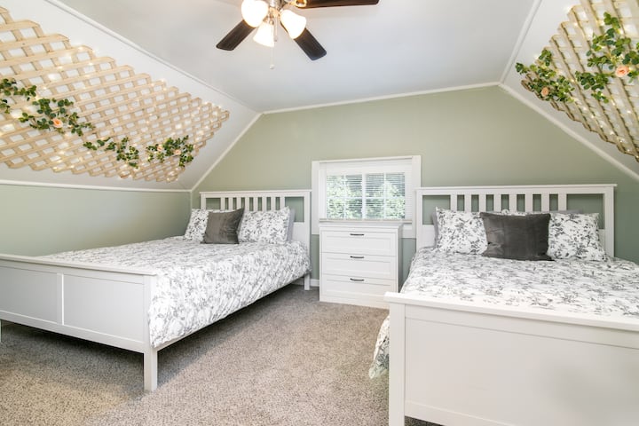 Bienvenue dans la chambre Rose ! Situé au 3e étage avec une salle de bain complète, ce charmant espace dispose d'un thème de roses de jardin, de 2 lits queen size et de murs en treillis en pente ornés de guirlandes lumineuses.