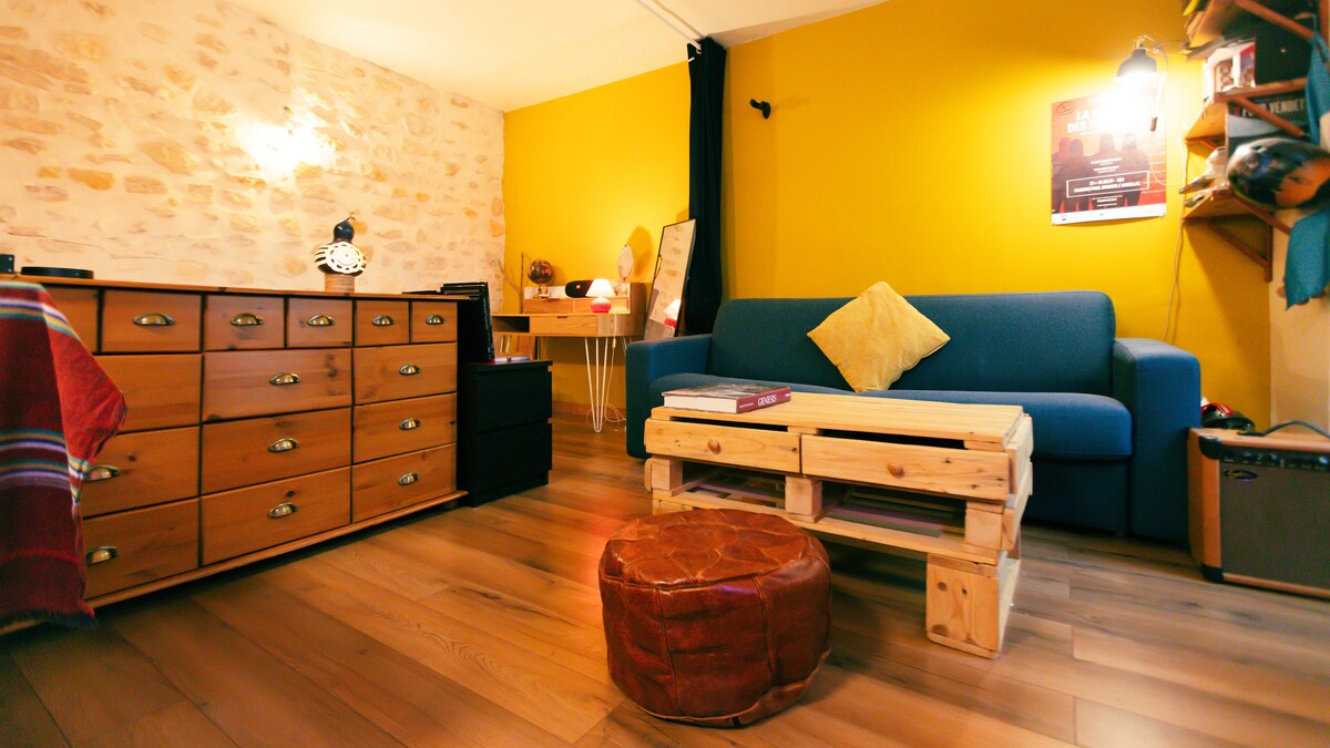 A cozy living space features a blue sofa adorned with a yellow cushion, accompanied by a handcrafted wooden coffee table. A wooden dresser with multiple drawers provides storage. Yellow and neutral walls create a warm ambiance, enhanced by natural wood flooring.