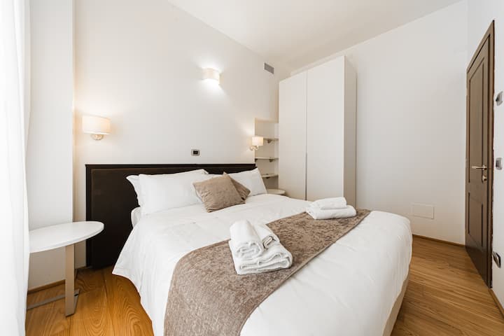 Amplio dormitorio con vista exclusiva a la calle principal en el centro de Bolonia. Los elementos elegantes y de diseño se combinan perfectamente con un entorno histórico, creando un ambiente refinado y cómodo.