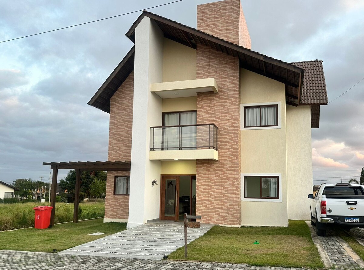 A three-story building features a modern design with a combination of brick and light-colored walls. A spacious front porch leads to a double door entrance. Large windows provide natural light, while a grassy area and a gravel pathway enhance the property's outdoor space.