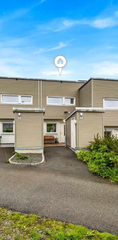 The exterior of the townhouse features a well-maintained facade with light-colored siding. A small, landscaped area with greenery frames the entrance, while a smooth pathway leads to the front door. Windows provide natural light, contributing to the overall inviting appearance.