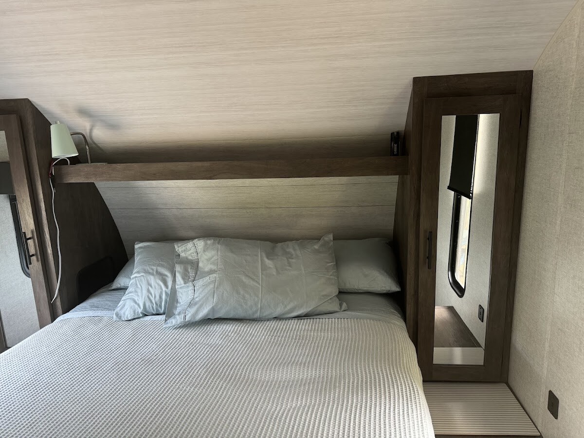 Ponemos un colchón queen completo en este espacio para mayor comodidad.  Hay enchufes USB, un televisor inteligente, armarios pequeños a cada lado y cortinas opacas.  Una puerta separa este espacio del resto de la caravana.  Las sábanas y la manta son de algodón y cómodas.