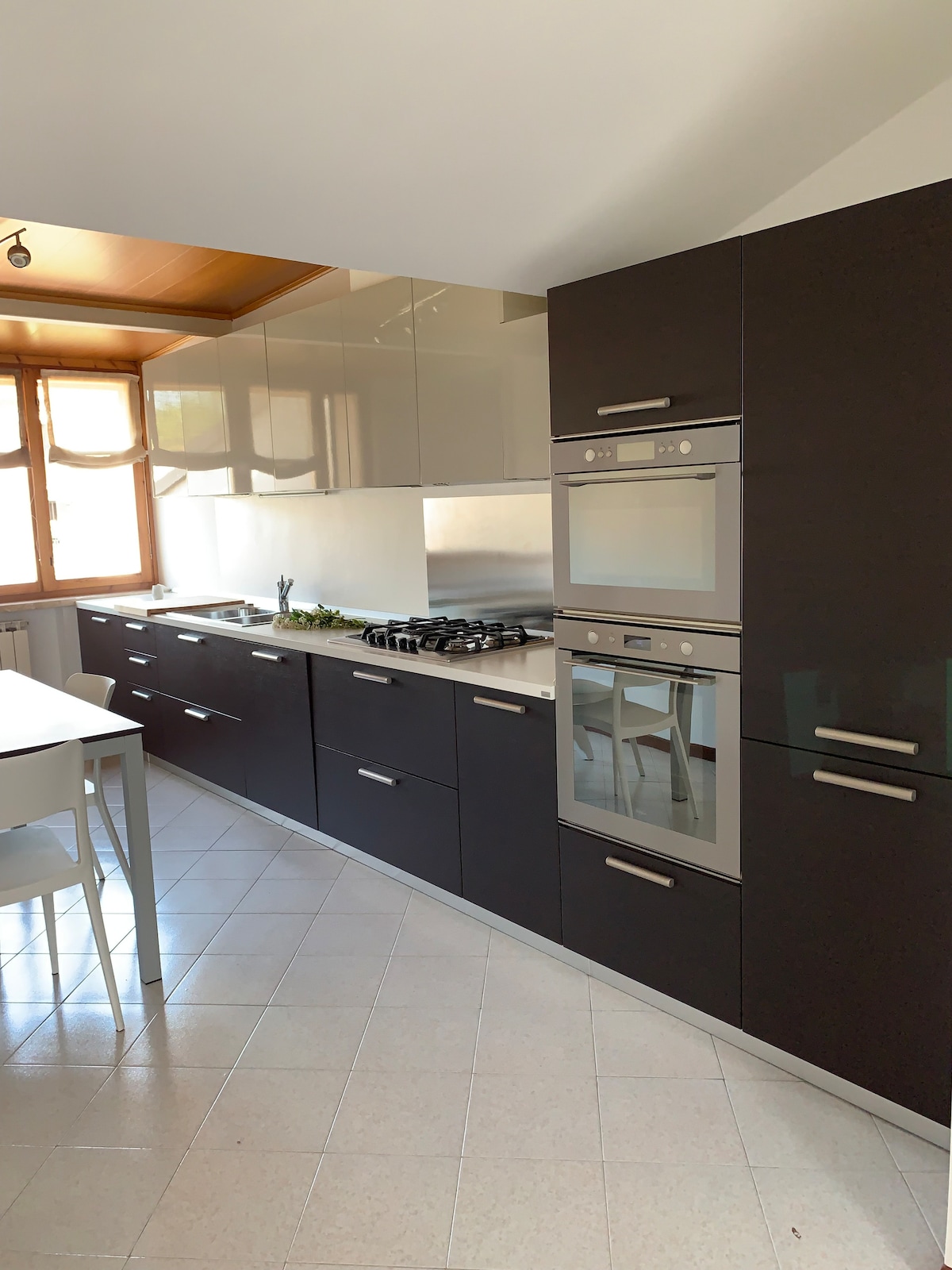 A contemporary kitchen is featured, showcasing dark cabinetry and sleek countertops. Built-in ovens and a stovetop are positioned alongside the ample cabinet space. A window allows natural light to illuminate the area, complementing the modern design.