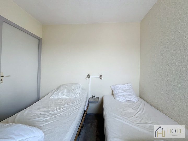 Мирна спална соба со удобен бел единечен кревет. Ве очекуваат меки сиви крпи, облеани во природна светлина од прозорецот. Спокојно одморалиште за мирна ноќ.