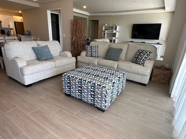 A spacious living area is furnished with a light-colored sofa and a patterned ottoman. Soft throw pillows are placed on the couch. Natural light enters through large glass doors, complementing the tile flooring and neutral walls.