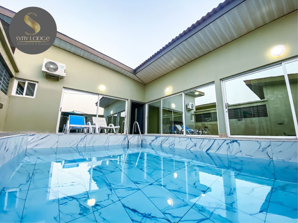 A private swimming pool is featured, with clear blue water reflecting the surrounding area. Large glass doors provide visibility into the villa's interior, enhancing the feeling of openness. Lounge chairs are positioned nearby for relaxation, creating an inviting environment.