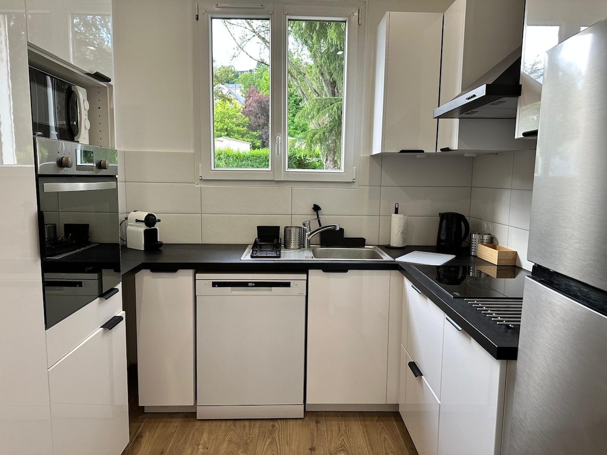 A modern kitchen features sleek white cabinetry with black countertops. Stainless steel appliances, including an oven, microwave, and refrigerator, are positioned for convenience. A window provides natural light, while the layout includes ample storage and workspace.