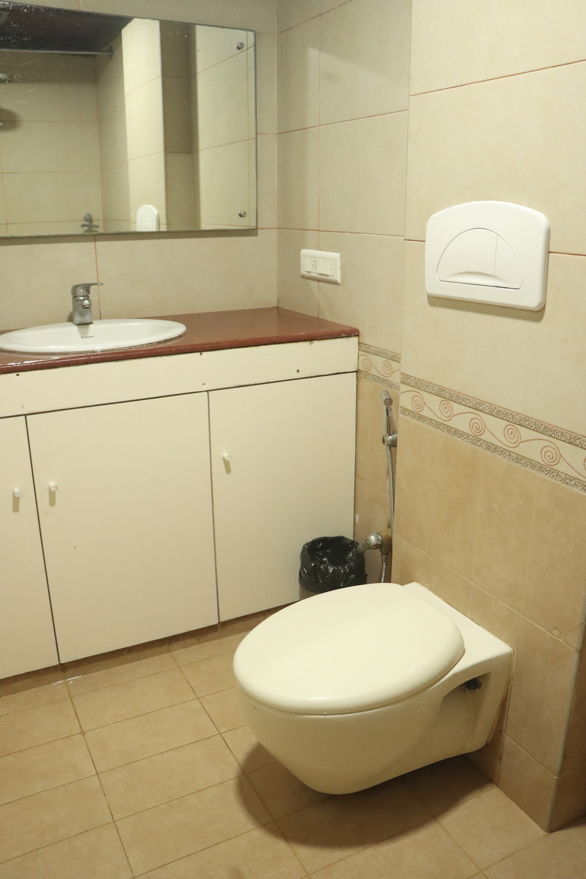 A clean bathroom is featured with tiled walls and a neutral color palette. A white toilet is positioned beside a spacious sink and a large mirror above it. Cabinet storage is provided underneath the sink for toiletries.