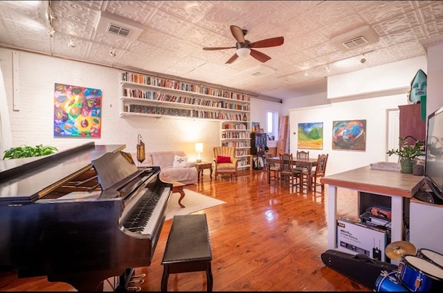 An open living area is highlighted by a grand piano and a collection of books displayed on wall-mounted shelves. Colorful artwork adorns the walls, while polished wooden flooring complements the space. A comfortable seating area invites relaxation alongside a dining table with chairs.