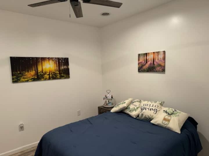 นี่คือห้องธีมฤดูร้อนเตียงควีนไซส์ 1 เตียงพร้อมโต๊ะข้างเตียงโคมไฟอ่านหนังสือพัดลมเพดานและตู้เสื้อผ้า โครงเตียงสูงพอที่จะเก็บสัมภาระไว้ใต้เตียงได้