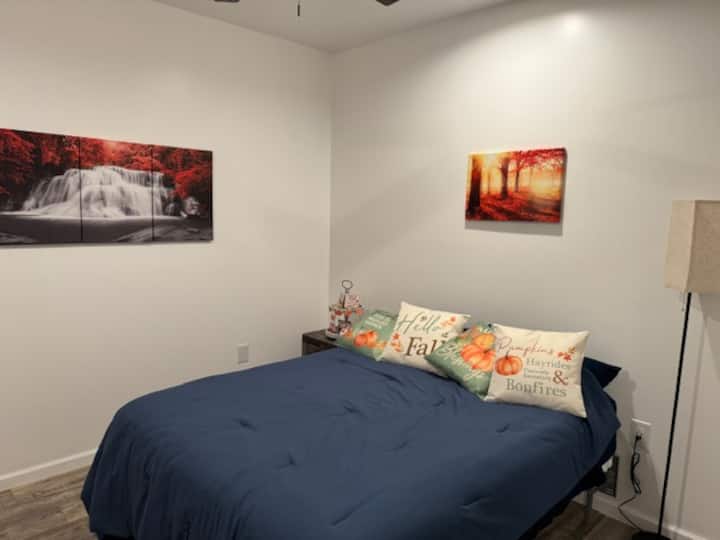 นี่คือห้องธีมฤดูใบไม้ร่วงเตียงควีนไซส์ 1 เตียงพร้อมโต๊ะข้างเตียงโคมไฟอ่านหนังสือพัดลมเพดานและตู้เสื้อผ้า โครงเตียงสูงพอที่จะเก็บสัมภาระไว้ใต้เตียงได้