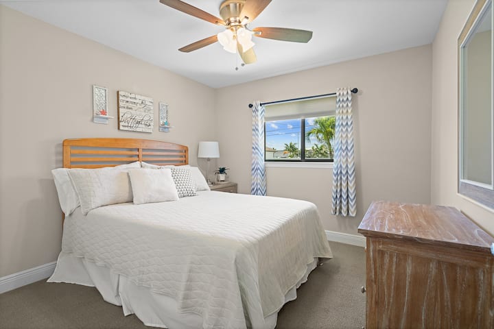 Kualika chumba cha wageni cha malkia kilicho na matandiko laini, mapambo ya kufurahisha na mwonekano wa dirisha wa mandhari ya kitropiki.