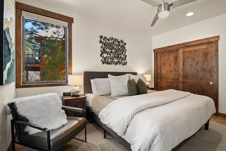 This serene king bedroom features plush bedding, organic textures, and large windows with forest views—your perfect retreat in Tahoe.