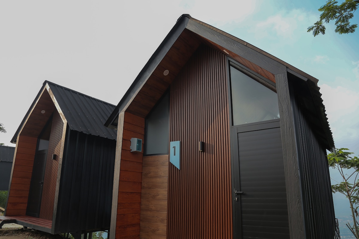 Two stylish cabins are displayed, featuring modern wooden exteriors with vertical panels. Cabin number one is highlighted with a blue numeral against a brown wood finish. Large windows offer ample natural light, while the sloped roofs add to the contemporary design.