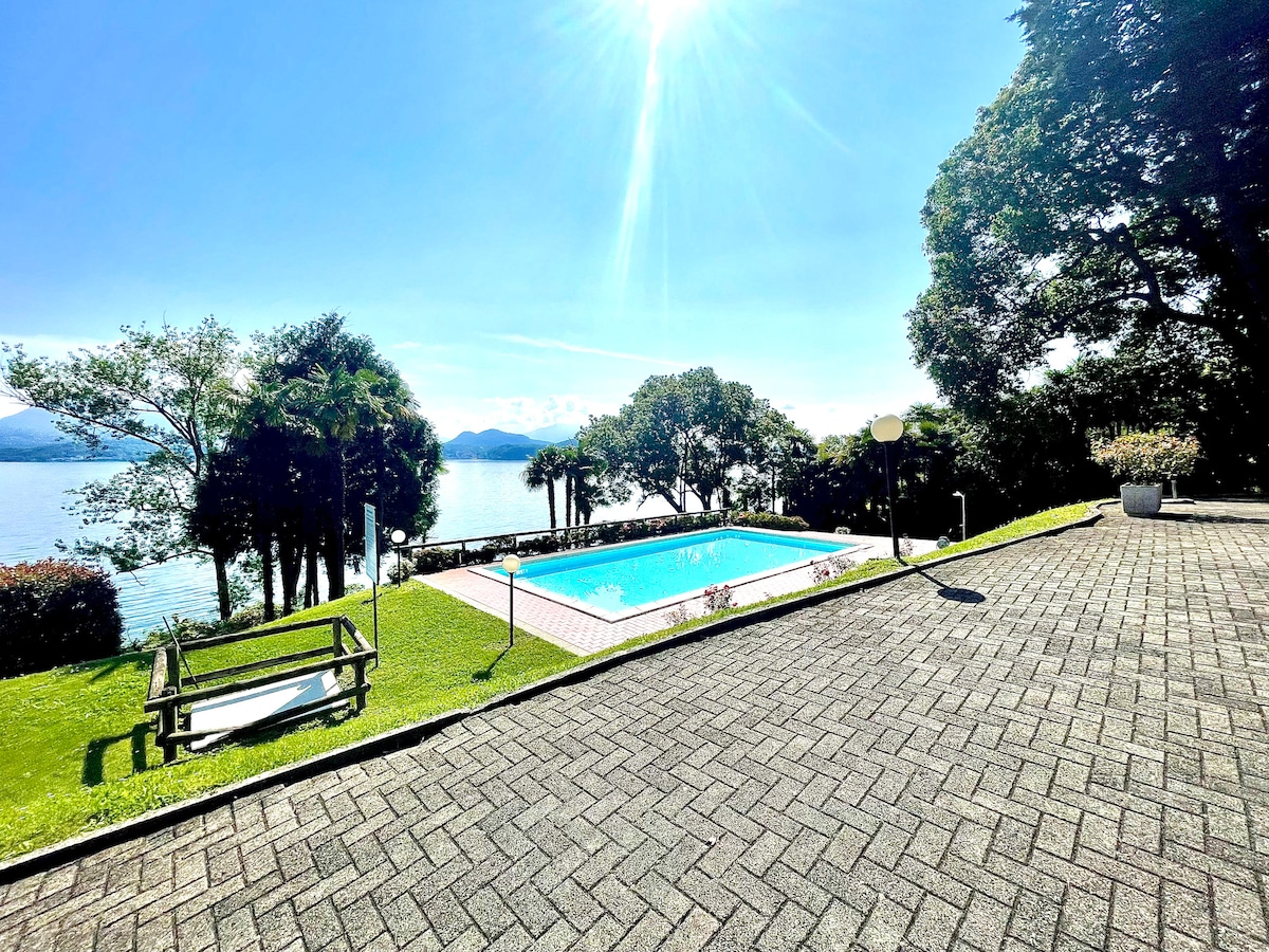 A private swimming pool is surrounded by lush greenery, with panoramic views of the water in the distance. Sunlight reflects off the clear water, and lounge chairs are positioned nearby for relaxation. The paved area provides ample space for outdoor activities.