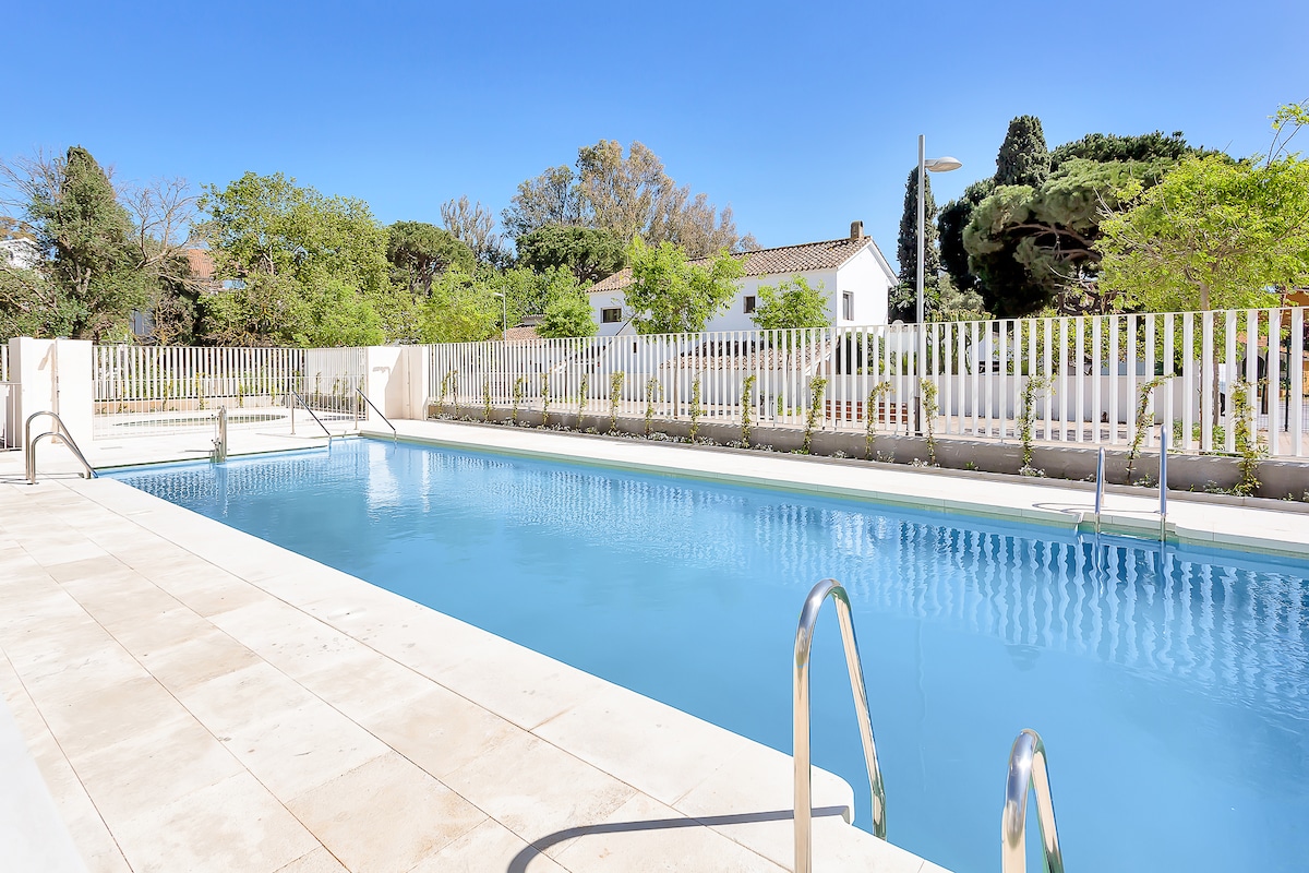 A clean and inviting swimming pool is framed by a spacious deck and surrounded by lush greenery. Several lounge chairs are set nearby, and a white fence offers privacy while allowing natural light to illuminate the area.