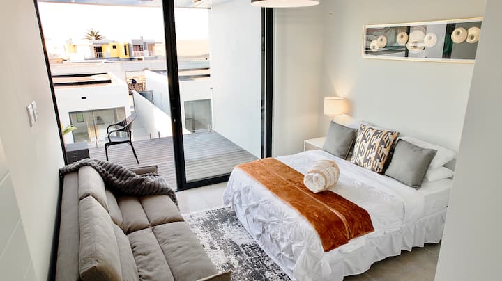 Სასტუმრო ოთახი Queen ‑ ის ზომის საწოლით და კომფორტული საძინებლის ტახტით. Აქვს აივანი ქვიშის ხედით. 