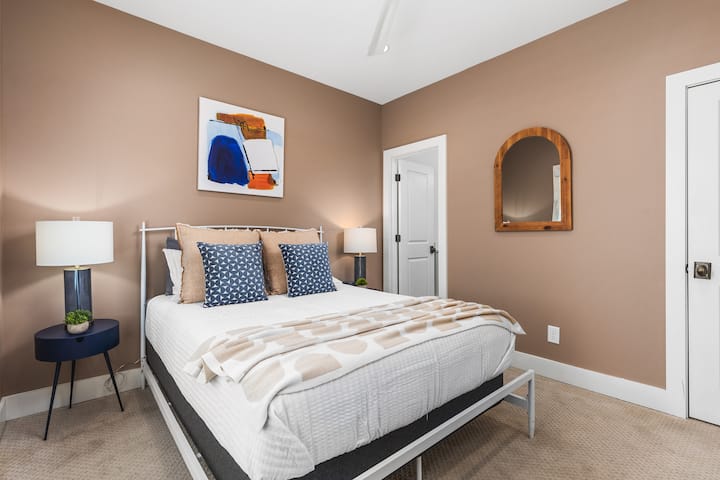 Საძინებელი №1 პირველ სართულზე, რომელშიც არის ორადგილიანი საწოლი, კარადა, ჭერის ვენტილატორი, ოთახის გამუქებული ფერები და სრული ზომის სააბაზანო.