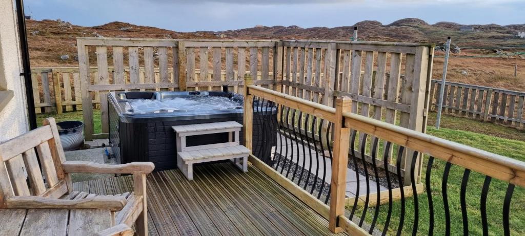A private deck area is featured, showcasing a hot tub surrounded by wooden fencing. A small step leads to the hot tub, while wooden seating is positioned nearby. The landscape beyond is characterized by rolling hills and open terrain, creating a spacious outdoor atmosphere.