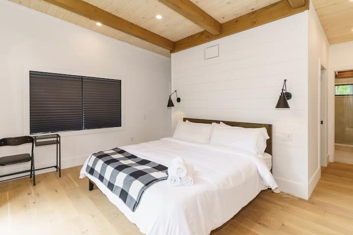 غرفة نوم حديثة ومريحة مع سرير أبيض، وأرضيات خشبية، ونافذة مع ستائر سوداء. تم تزيين الغرفة ببساطة وتتمتع بأجواء هادئة. إنه المكان المثالي للاسترخاء والاسترخاء بعد يوم طويل.