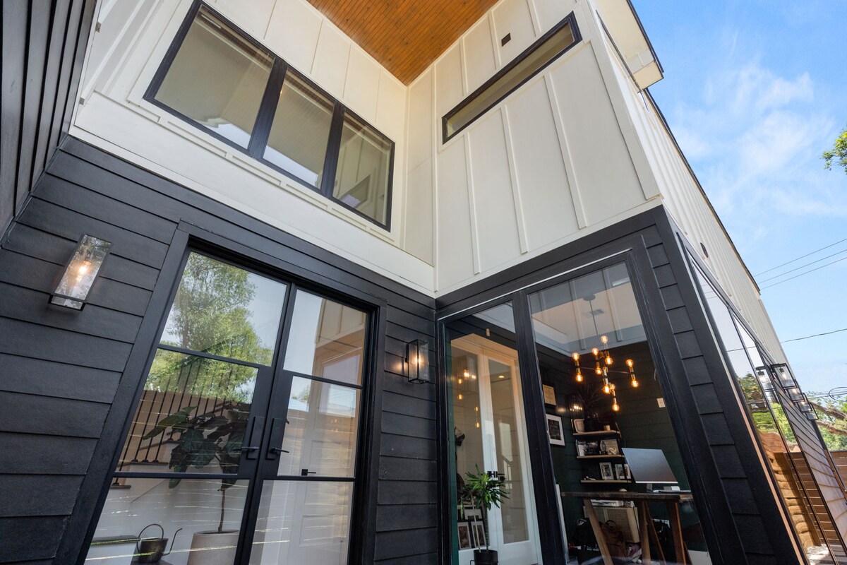 The exterior of the home showcases a blend of contemporary design and sleek lines. Large windows provide ample natural light, while the dark and light color contrast creates an attractive facade. An outdoor seating area is visible near the entrance.