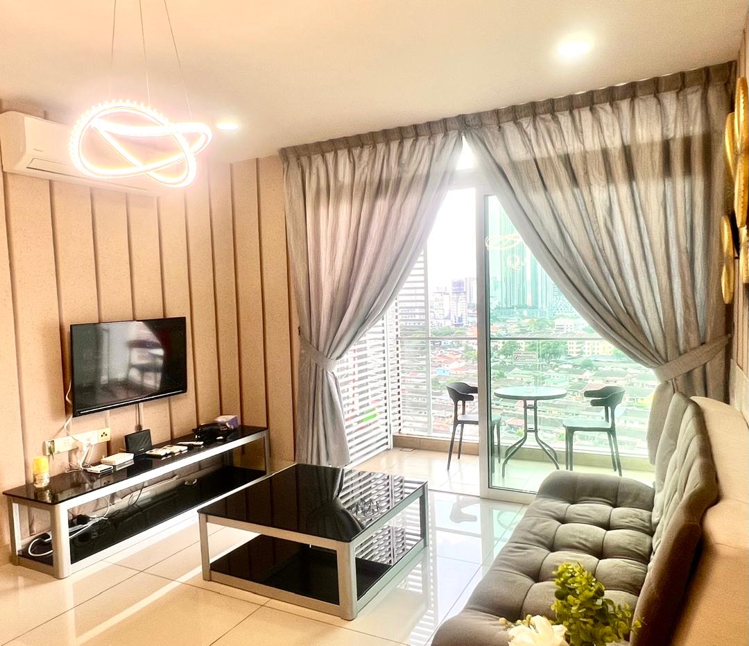 The living room features a comfortable sofa and a sleek coffee table, with a TV cabinet situated below a modern LED TV. Large windows covered with elegant curtains allow natural light to fill the space, revealing a balcony with an urban view.