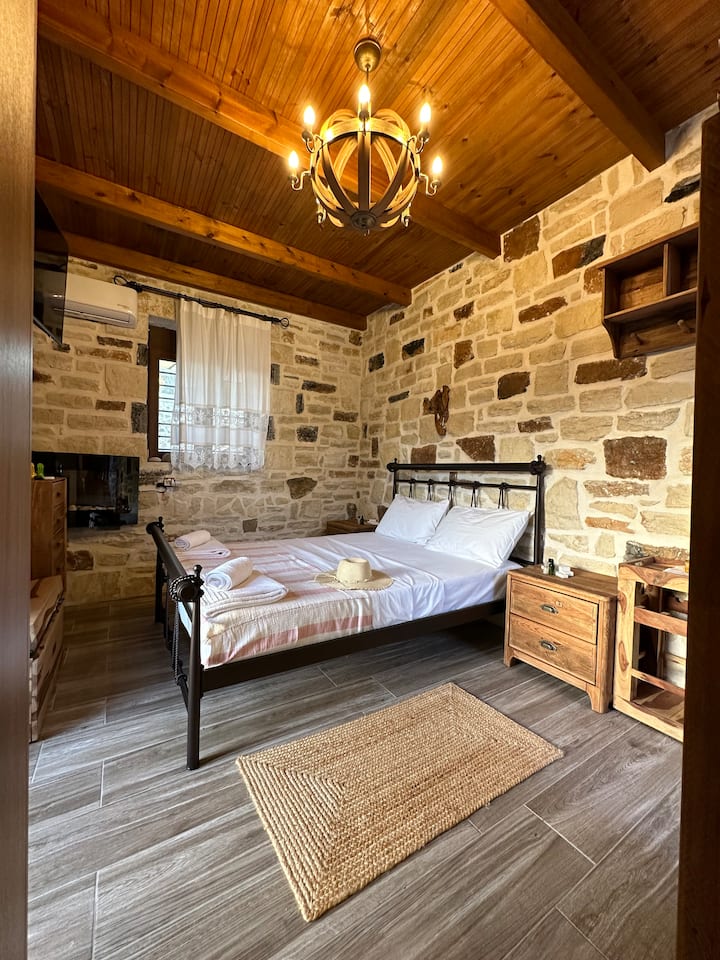 El dormitorio combina bellamente el encanto tradicional con las comodidades modernas. Las paredes de piedra agregan un toque rústico, mientras que la acogedora cama doble, el aire acondicionado contemporáneo y la iluminación suave garantizan una estancia lujosa y cómoda.