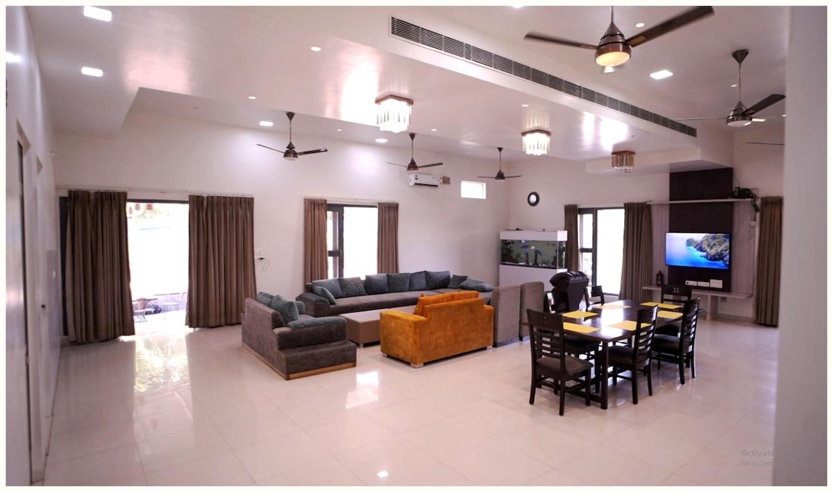 A spacious living area showcases a large sectional sofa, complemented by a bright yellow accent chair. A dining table for six is positioned nearby, with sliding glass doors allowing natural light and access to the outdoor area. Ceiling fans enhance comfort throughout the space.