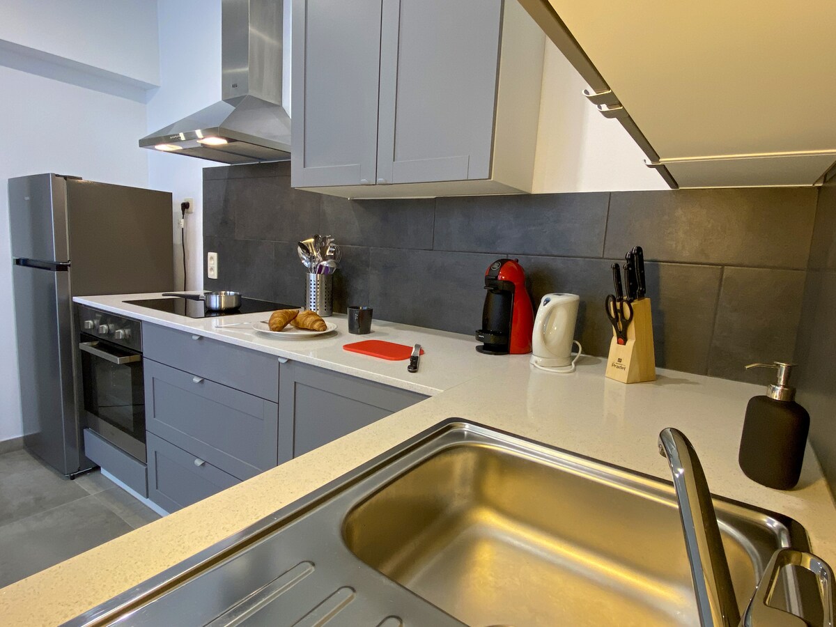 A fully equipped kitchen is presented, featuring modern cabinetry and a spacious countertop. Appliances include a refrigerator, oven, and stovetop, complemented by a coffee machine and kettle. Various utensils are organized neatly, enhancing the cooking experience.