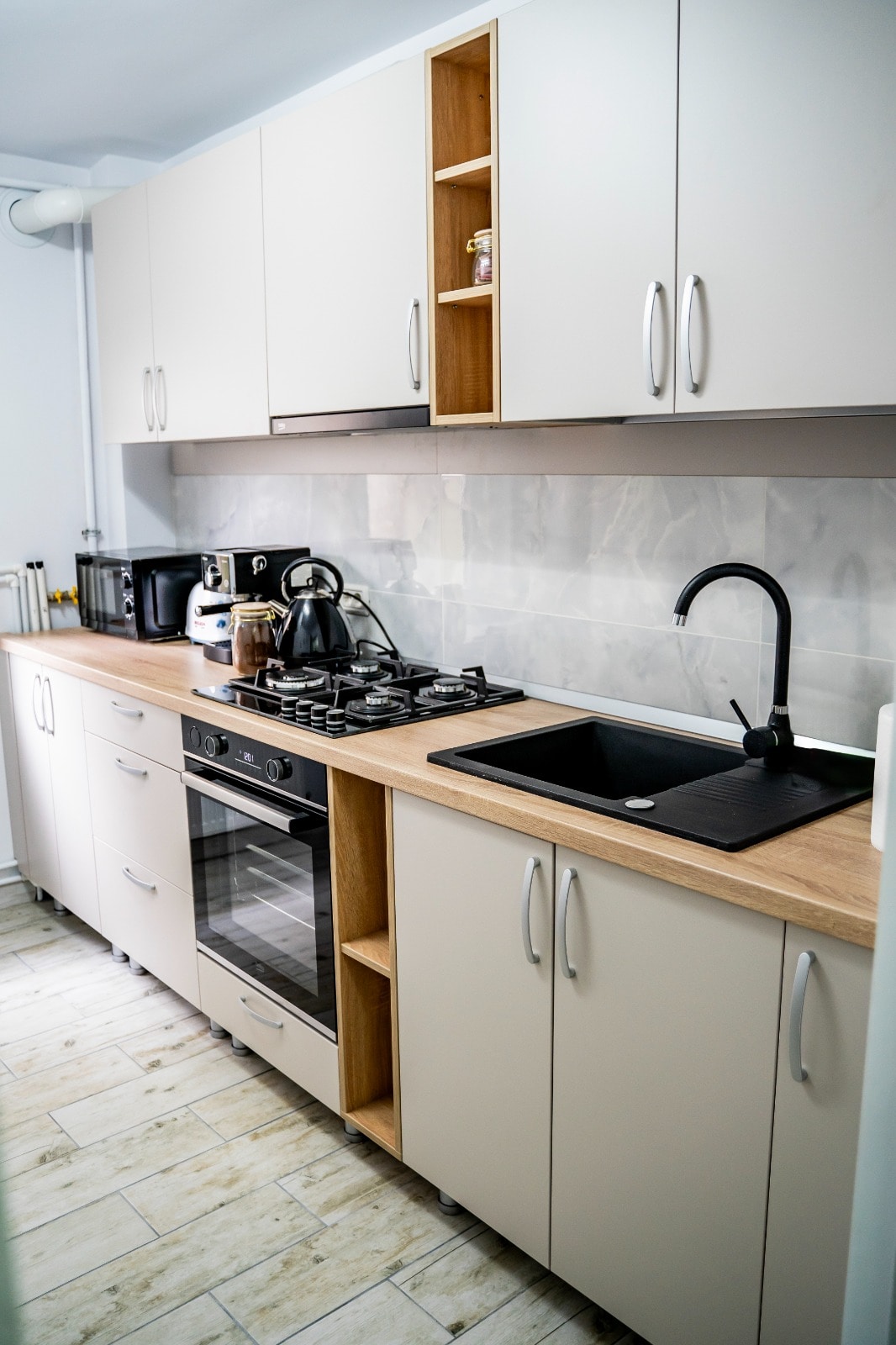 The kitchen is equipped with modern cabinetry, featuring wooden accents. A stainless steel oven and a gas stove are present, alongside a sleek black sink. Essential appliances, including a kettle and coffee maker, are arranged conveniently on the countertop.