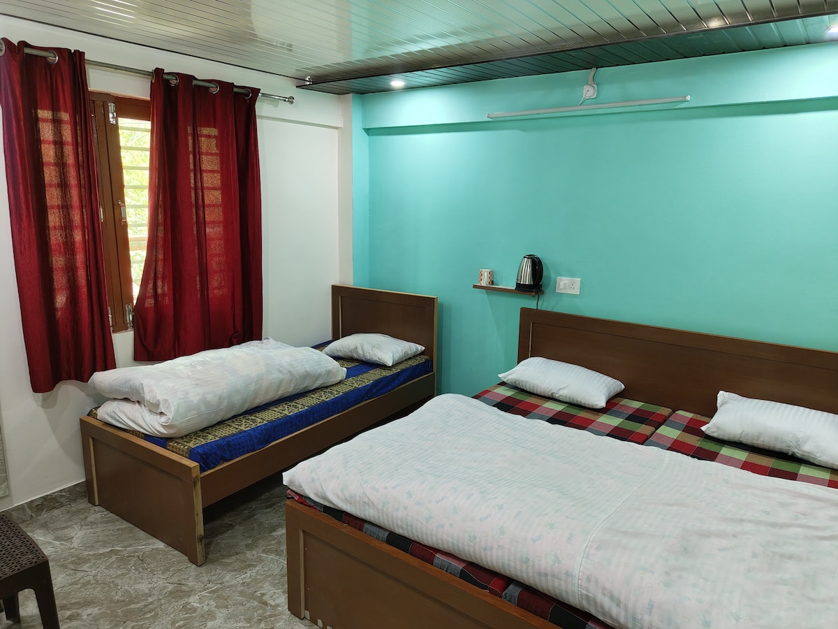 A bright sleeping area features two wooden beds dressed with light bedding. Red curtains frame the window, allowing natural light to brighten the room. A kettle is placed on a shelf, and a patterned chair adds a touch of comfort to the space.