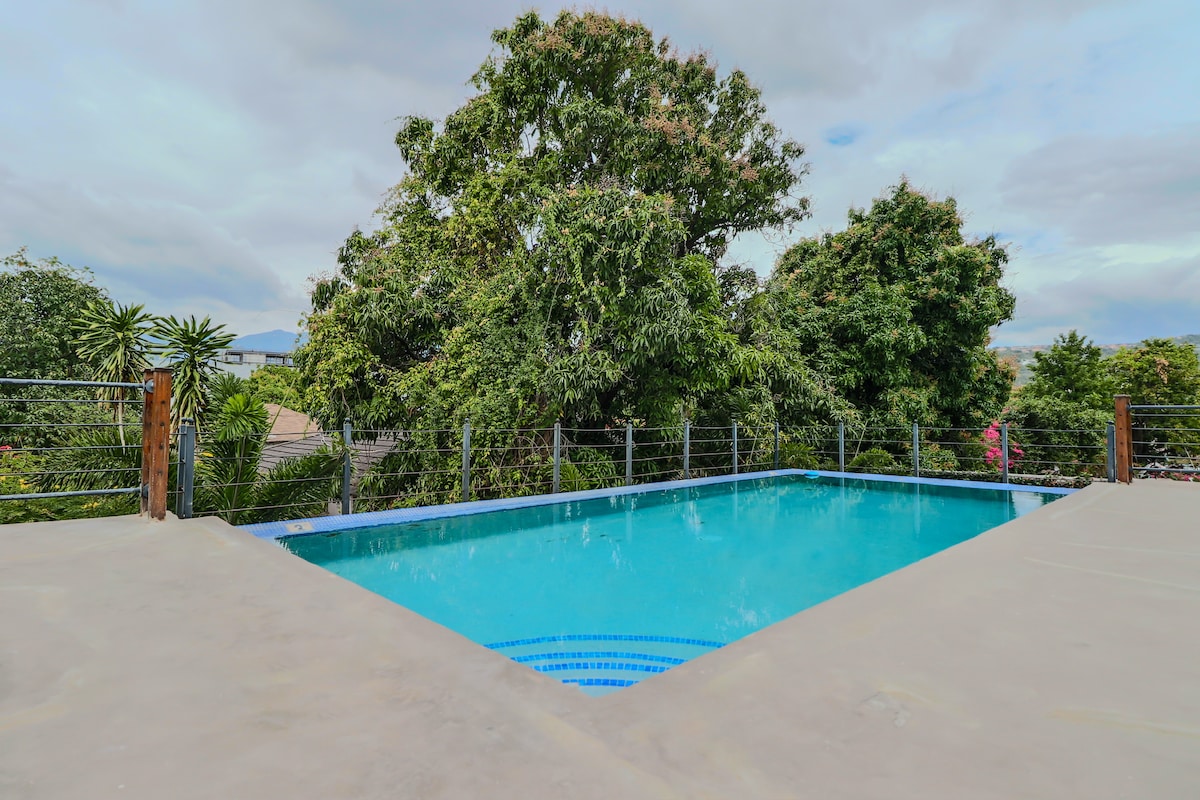 A private pool is surrounded by lush greenery, offering a serene environment for relaxation. The pool's clear blue water reflects the sky, while a wooden railing adds a natural touch. Nearby trees provide shade, enhancing the tranquil outdoor setting.
