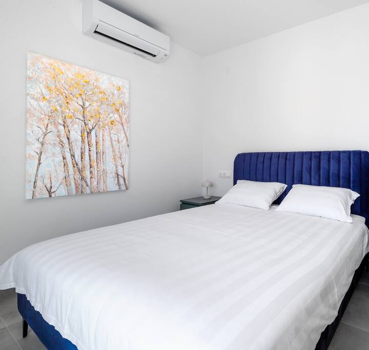 ダブルベッド、エアコン、テレビ、海とオリーブガーデンビューのバルコニー付きの寝室。電気ブラインドが含まれています。