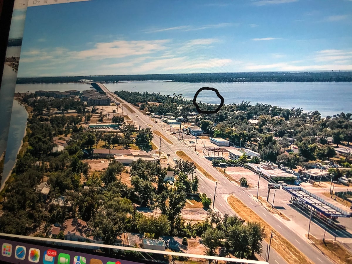 An aerial view captures a stretch of roadway alongside a tranquil water body. Lush greenery encompasses the area, with a mix of residential and commercial properties visible. The location's proximity to the water is highlighted, providing a sense of accessibility to nearby waterways.