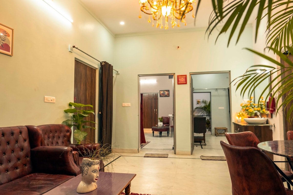 An inviting entry area is seen, featuring a comfortable brown leather sofa and a round table. The space is enhanced by soft lighting and greenery, with open doors leading to other rooms in the background, creating a welcoming and spacious atmosphere.