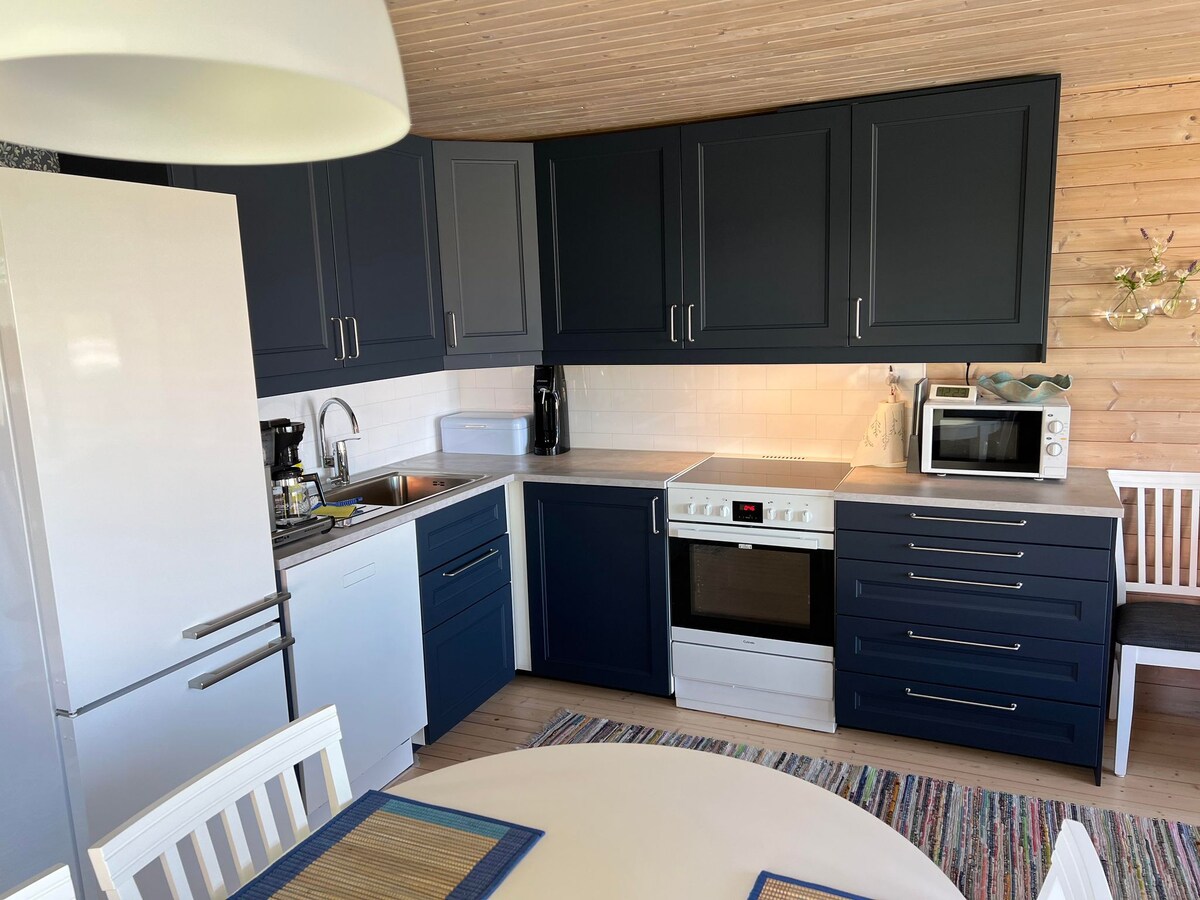 A functional kitchen showcases dark blue cabinets accompanied by a white countertop. Essential appliances include a refrigerator, stove, microwave, and coffee maker. A round dining table is set with placemats, enhancing the kitchen's practicality and inviting atmosphere.