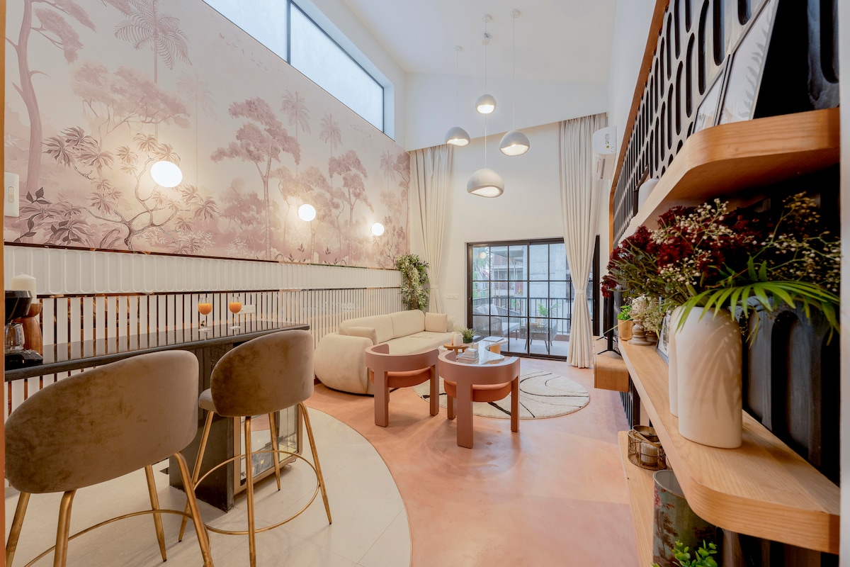 A spacious living area features a contemporary lounge with a plush sofa and round coffee table. Large windows allow natural light to fill the space, while artistic wallpaper adds a touch of elegance. A dining table with soft, rounded chairs accommodates guests comfortably.