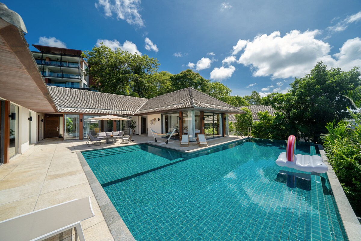 The outdoor area features a private swimming pool, surrounded by lush greenery. Comfortable lounge chairs are positioned near the water, offering a serene space for relaxation. A patio with a shaded seating area provides a welcoming spot to enjoy sunny days.