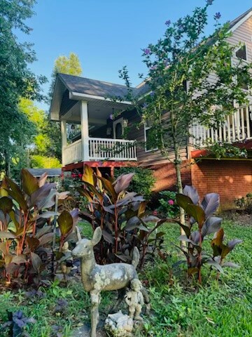 The exterior of the home is highlighted by a charming front porch with white railings. Lush greenery and colorful plants surround a decorative deer sculpture, contributing to the tranquil setting. Morning sunlight illuminates the scene, creating a peaceful atmosphere.