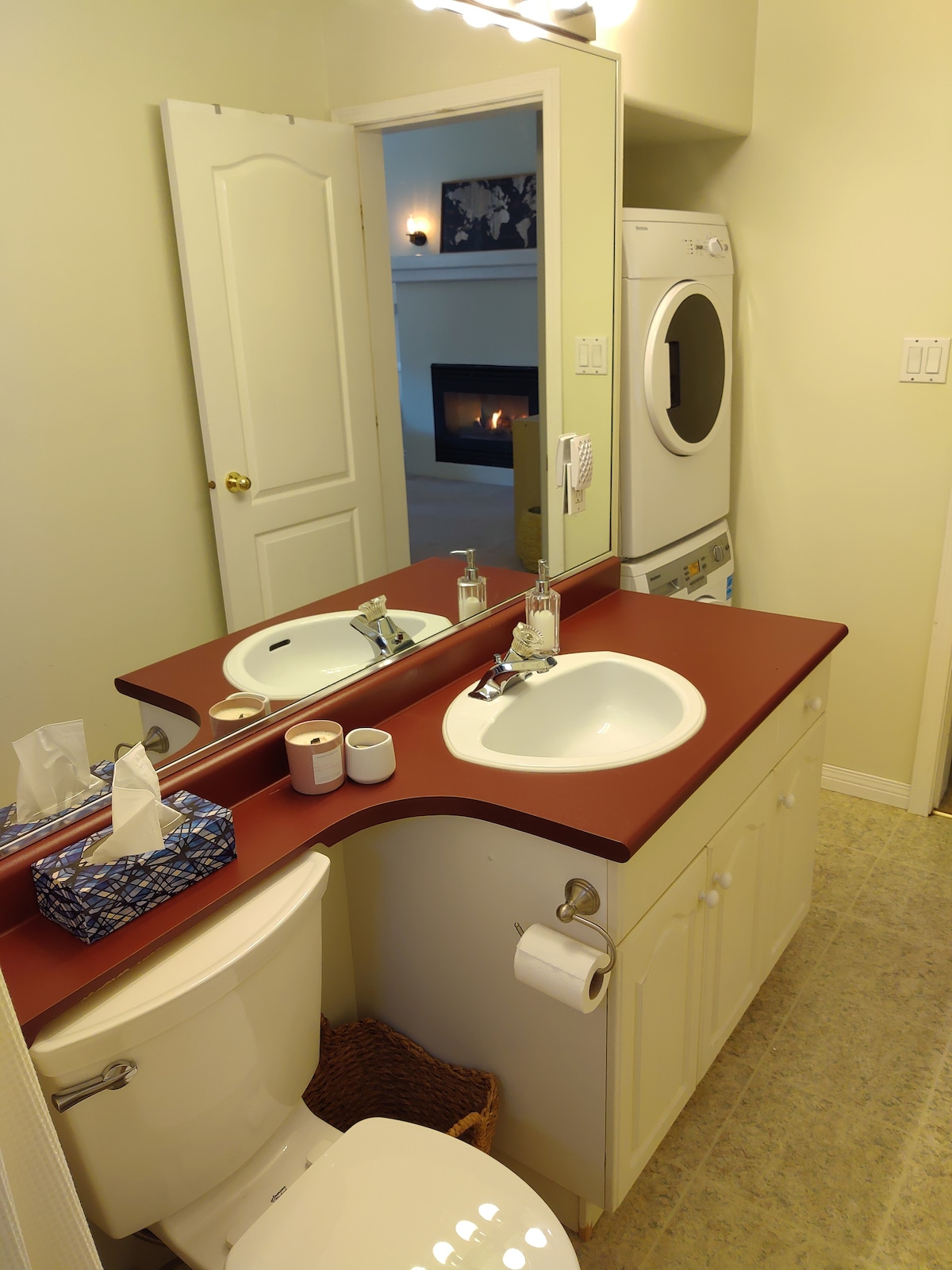 A well-organized bathroom is shown, featuring a white sink with a modern faucet, a toilet, and a laundry machine. The counter is equipped with basic toiletries and a tissue box. Soft lighting creates a functional and tidy atmosphere.