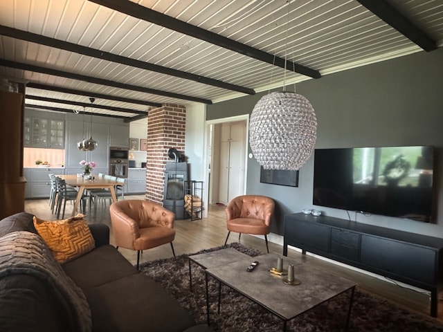 A spacious living area features a large sectional sofa and two leather armchairs, providing ample seating. A television is mounted on the wall opposite a stylish coffee table. Exposed wooden beams add character to the ceiling, while a dining table is visible in the background.